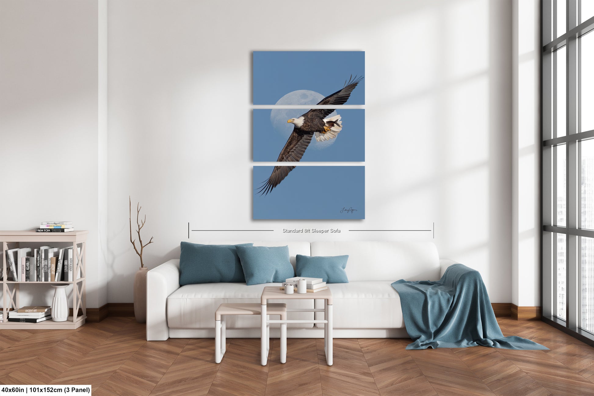 A modern living room with a white sofa, a coffee table, and a bookshelf. Above the sofa is a large canvas print depicting a bald eagle in flight against a blue sky with a full moon.