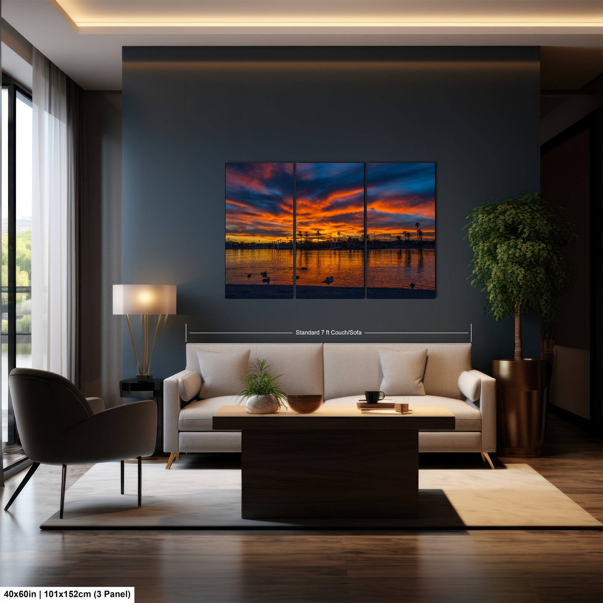 a modern living room with a large, three-panel landscape painting hanging on the wall. The painting features a sunset over a body of water, with silhouettes of trees and buildings visible in the background. The room is furnished with a white sofa, a coffee table, and a potted plant, creating a cozy and inviting atmosphere.
