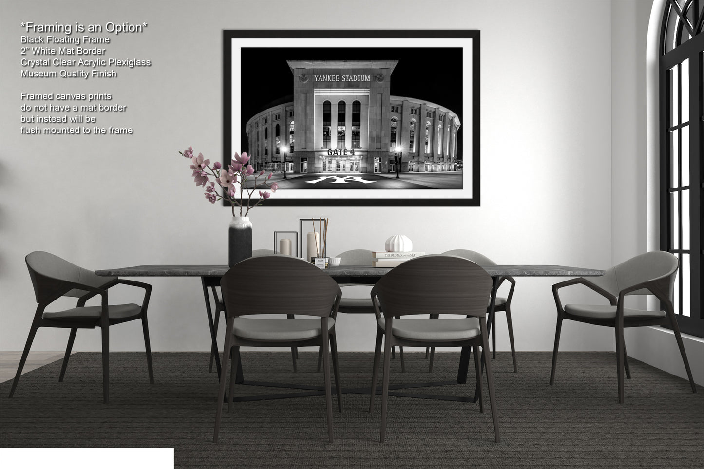a modern dining room with a large framed black and white photograph of a stadium on the wall. The photograph is framed in a black frame and is the focal point of the room. The dining table is surrounded by four chairs, and there is a vase of flowers on the table. The room has a minimalist and clean design, with white walls and a gray carpet.