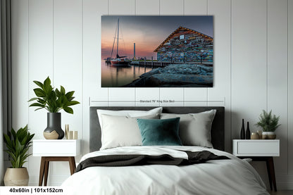 a serene scene of a wooden building with a dock and a sailboat, set against a beautiful sunset sky.