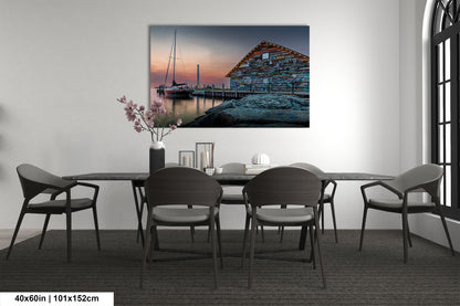 a serene scene of a boat docked at a pier, with a building featuring a colorful facade in the background. The photograph is framed and hung on a wall, creating a focal point in the room.