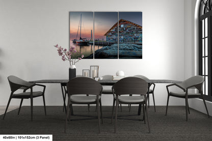 a modern dining room with a large, three-panel painting of a boat on a dock in the background. The painting is hung on the wall above a black dining table surrounded by six chairs. The room has a minimalist and contemporary design, with a vase of flowers and a book on the table adding a touch of color and personalization to the space.