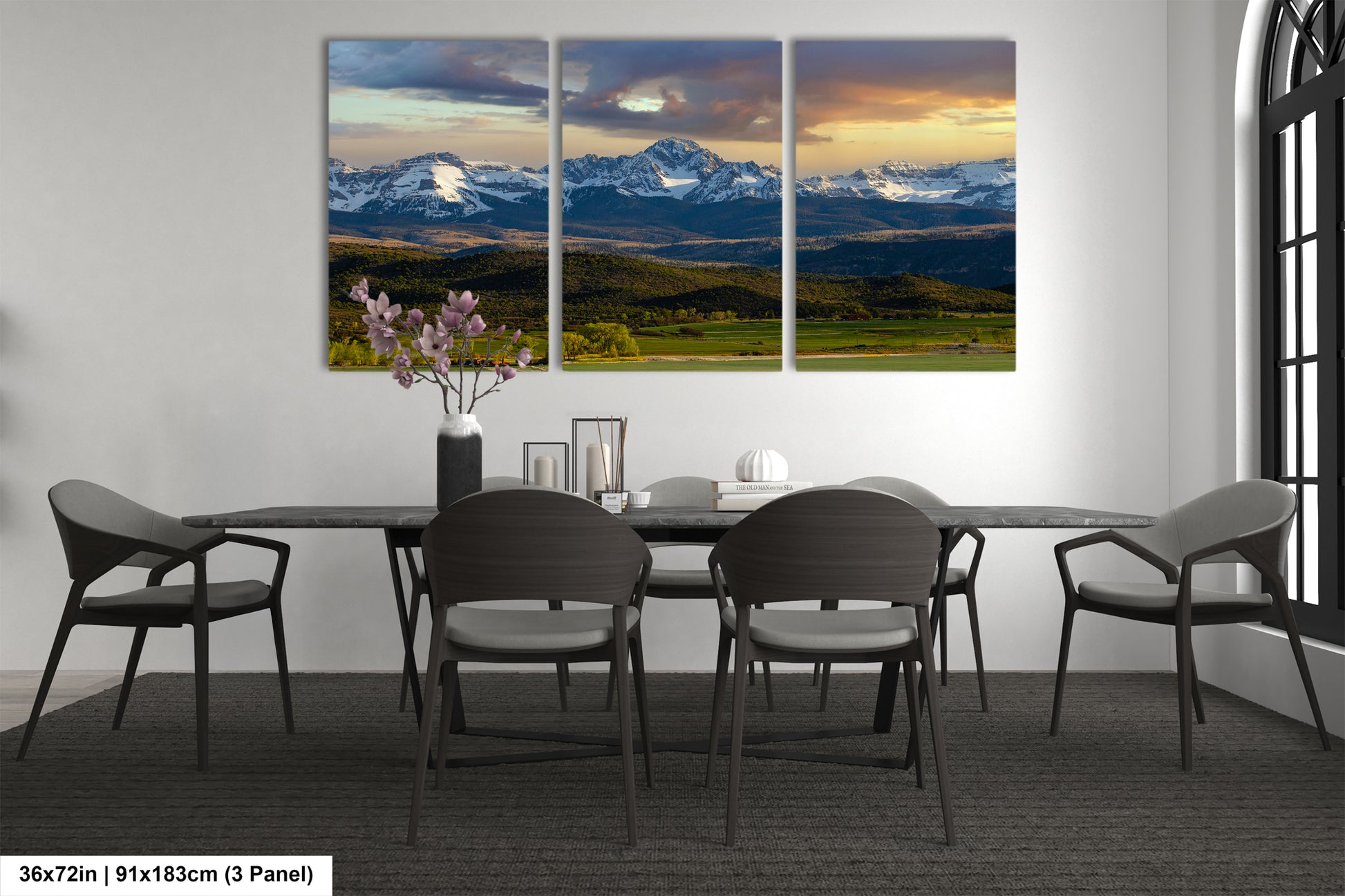 a modern dining room with a large, three-panel landscape painting of a mountain range above a table with chairs.