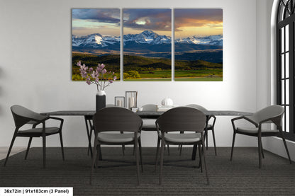 a modern dining room with a large, three-panel landscape painting of a mountain range above a table with chairs.