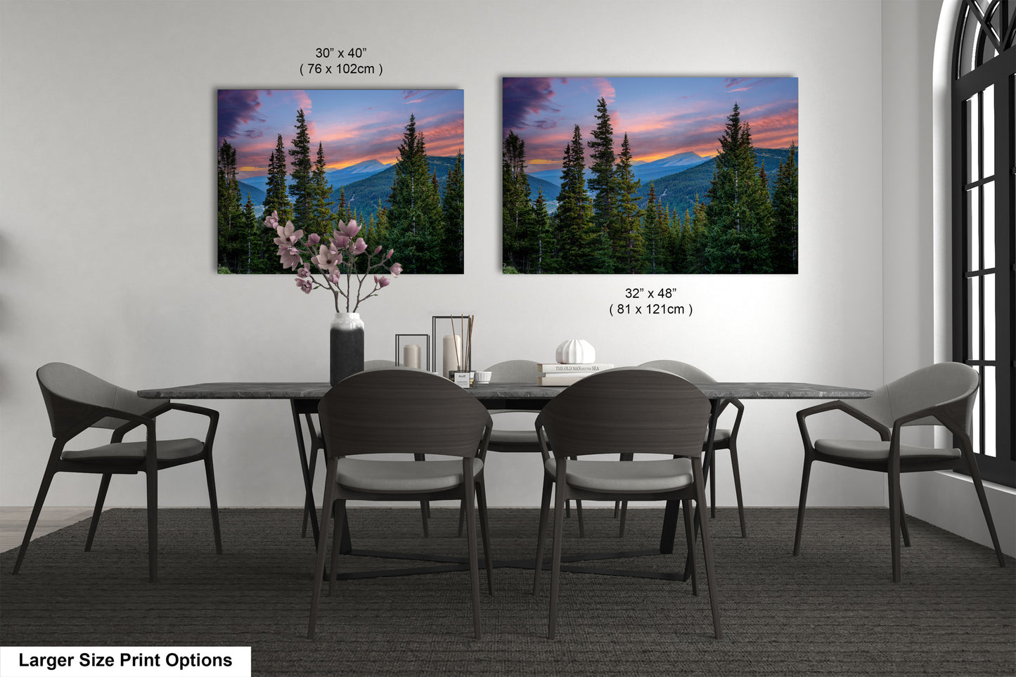 a dining room with a large dining table surrounded by chairs. There are two framed landscape photographs hanging on the wall above the table, depicting a scenic mountain landscape with pine trees and a colorful sunset.