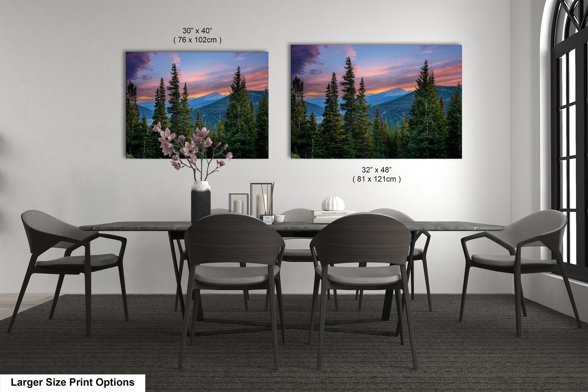 a dining room with a large dining table surrounded by chairs. There are two framed landscape photographs hanging on the wall above the table, depicting a scenic mountain landscape with pine trees and a colorful sunset.