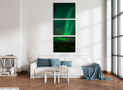 A modern living room with a white sofa, a coffee table, and a bookshelf. Above the sofa is a large, three-panel print depicting a night sky with the Aurora Borealis or Northern Lights.