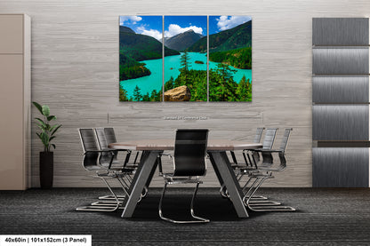 a modern office space with a large, three-panel landscape painting of a scenic mountain lake and forest on the wall. The painting is framed in a minimalist style and is the focal point of the room. The office has a sleek, contemporary design with gray walls and a gray carpeted floor. The table and chairs are arranged around the painting, creating a comfortable and inviting atmosphere for meetings or discussions.