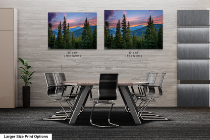 a modern office space with a large wooden table surrounded by black chairs. Above the table, there are two framed landscape photographs depicting a scenic mountain view at sunset. The photographs are of different sizes, with one being larger than the other. The office space has a minimalist design with gray walls and a gray carpet.