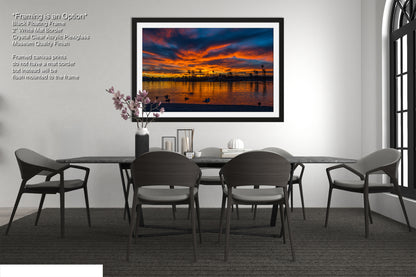 a modern dining room with a large framed picture of a sunset over a body of water hanging on the wall above a black dining table surrounded by six chairs.
