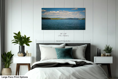 A large pano print depicting a serene landscape of a lake with mountains in the distance, surrounded by lush greenery.