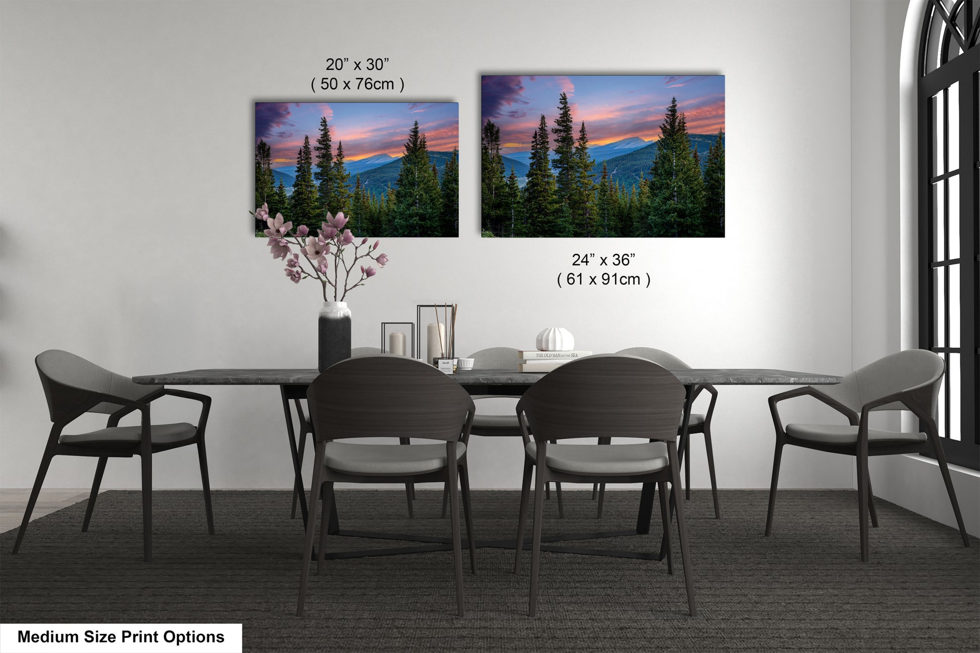 a dining room with a large dining table surrounded by six chairs. Above the table, there are two framed landscape paintings depicting a mountain range at sunset. The paintings are of different sizes, with one being larger than the other. The paintings are hung on the wall above the table, creating a focal point in the room.