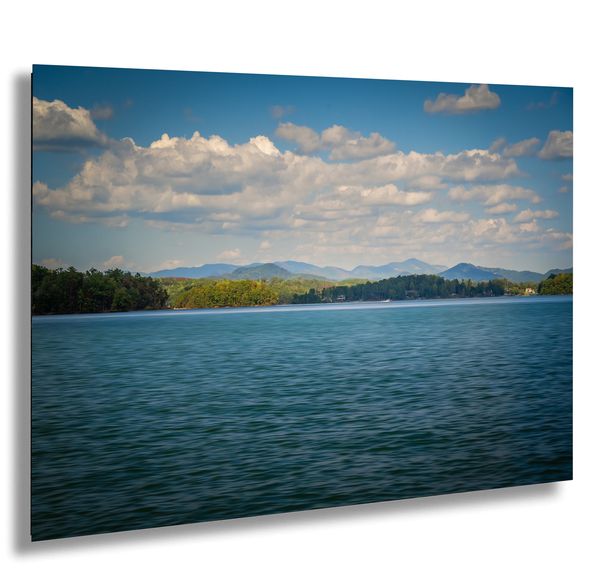 a serene lake surrounded by lush green trees and mountains, with a clear blue sky dotted with fluffy white clouds.