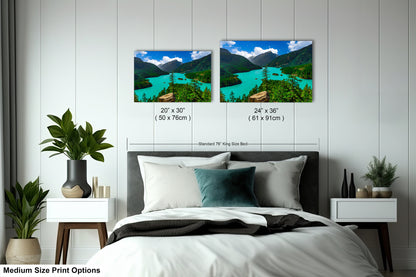 a bedroom with a bed, nightstands, and potted plants. There are two framed landscape photographs hanging on the wall above the bed, depicting a scenic mountain view with turquoise water.