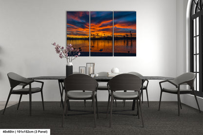 a modern dining room with a large, colorful painting of a sunset over a body of water hanging on the wall above a black table surrounded by six chairs.