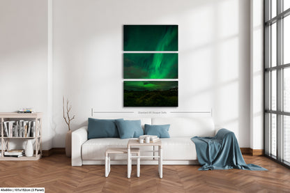 A modern living room with a white sofa, a coffee table, and a bookshelf. Above the sofa is a large canvas print depicting a night sky with the aurora borealis.
