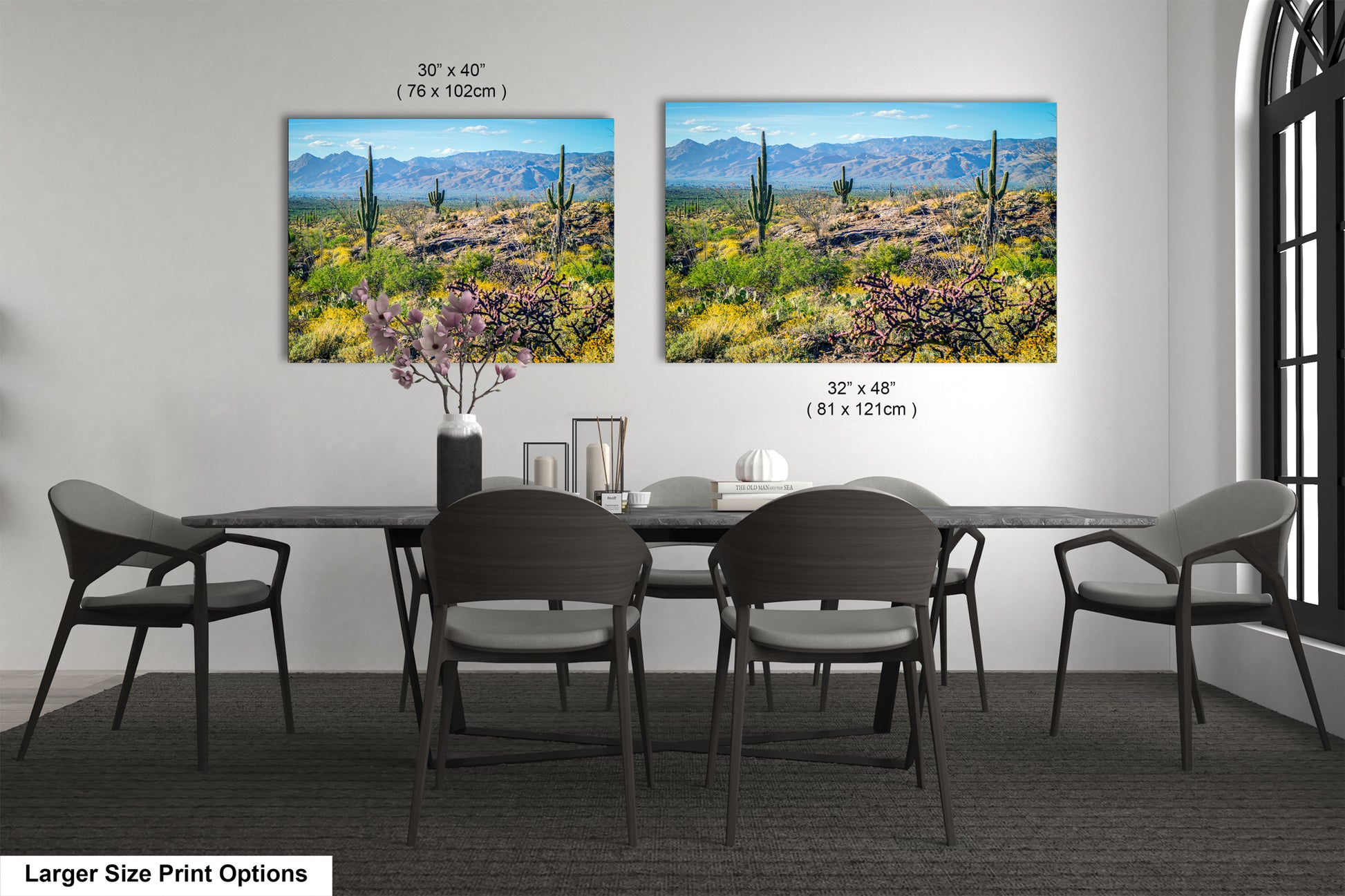 a modern dining room with a large dining table and six chairs. Two framed landscape paintings are displayed on the wall above the table, depicting a desert scene with mountains in the background.