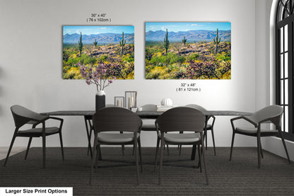 a modern dining room with a large dining table and six chairs. Two framed landscape paintings are displayed on the wall above the table, depicting a desert scene with mountains in the background.
