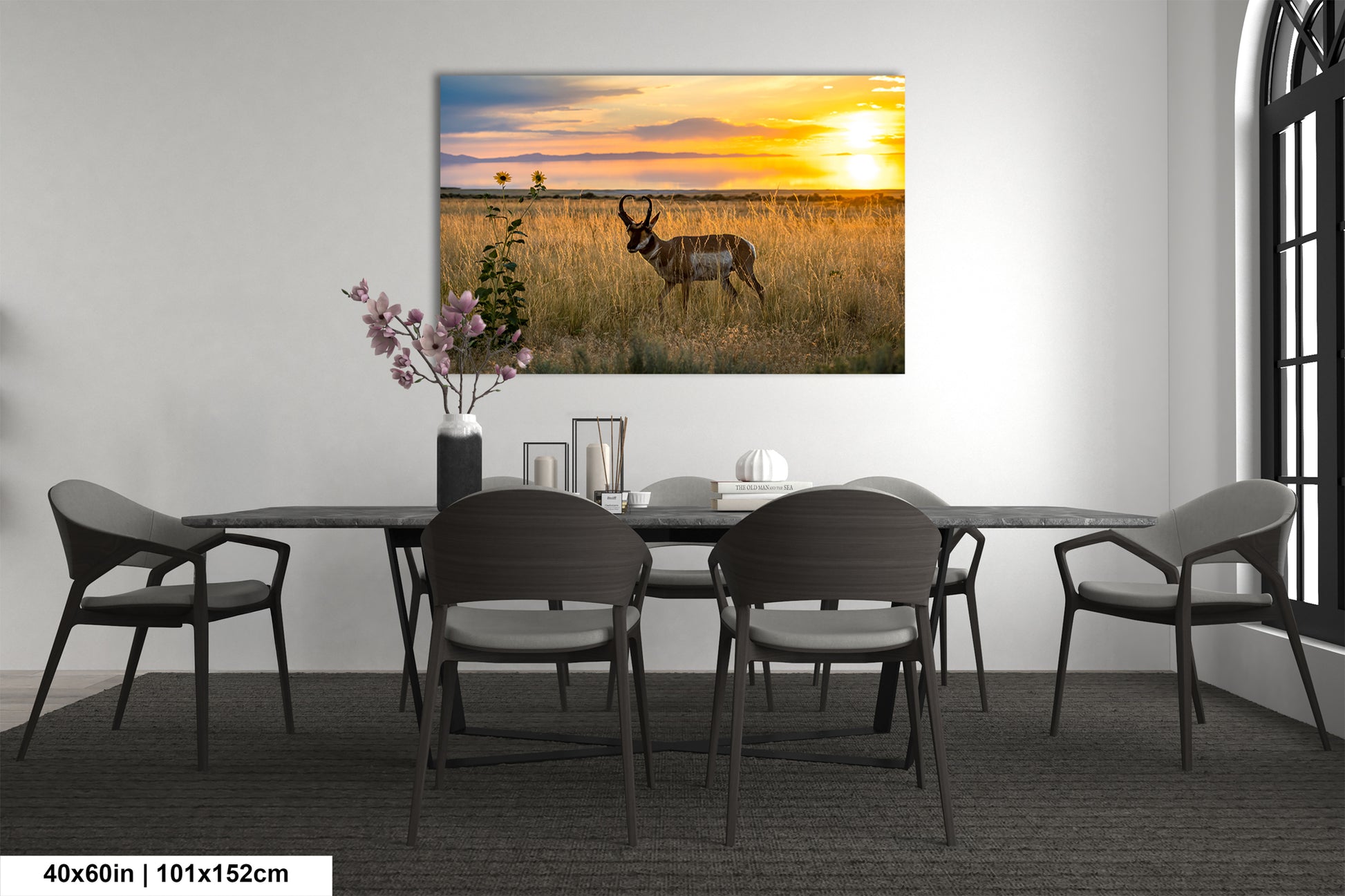 a large painting of a deer in a field with a sunset in the background, hanging on a wall above a dining table with chairs.