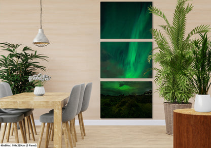 The image is a modern dining room with a wooden table and chairs, a hanging light fixture, and a large potted plant. The wall behind the table features three separate images of the Aurora Borealis, or Northern Lights, creating a visually striking and nature-inspired atmosphere.