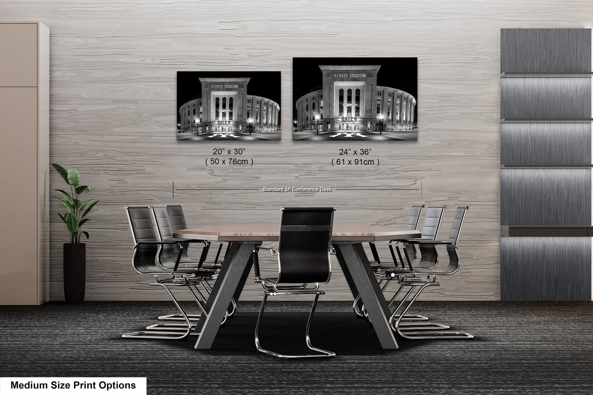 a modern office or conference room setting with a large wooden table surrounded by black chairs. There are two framed black and white photographs of a building displayed on the wall above the table. The photographs are of different sizes, with one being larger than the other. The room has a minimalist and contemporary design, with a gray wall and a plant in the corner.