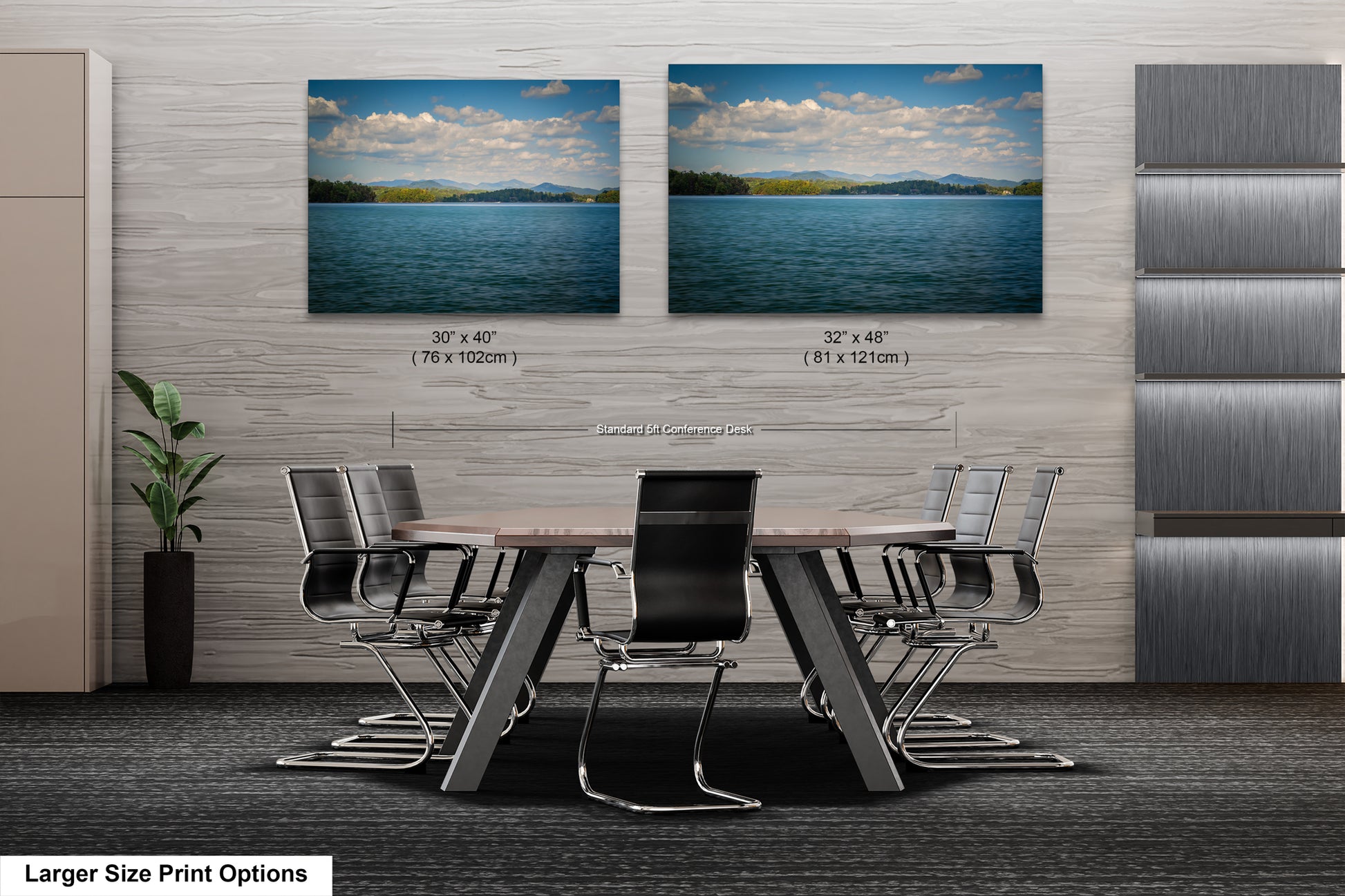 a modern office space with a large wooden table surrounded by black chairs. Two framed landscape paintings are displayed on the wall above the table, depicting a serene lake scene with mountains in the background.