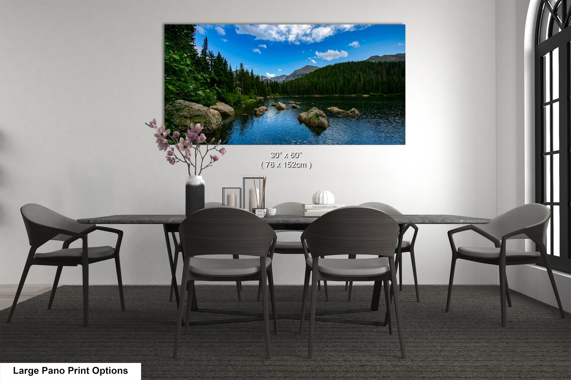 A large pano print depicting a serene landscape with a lake, mountains, and trees is displayed on the wall above a dining table with chairs.