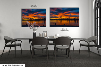 a dining room with a large dining table and six chairs. Two large paintings of a sunset scene are displayed on the wall above the table.