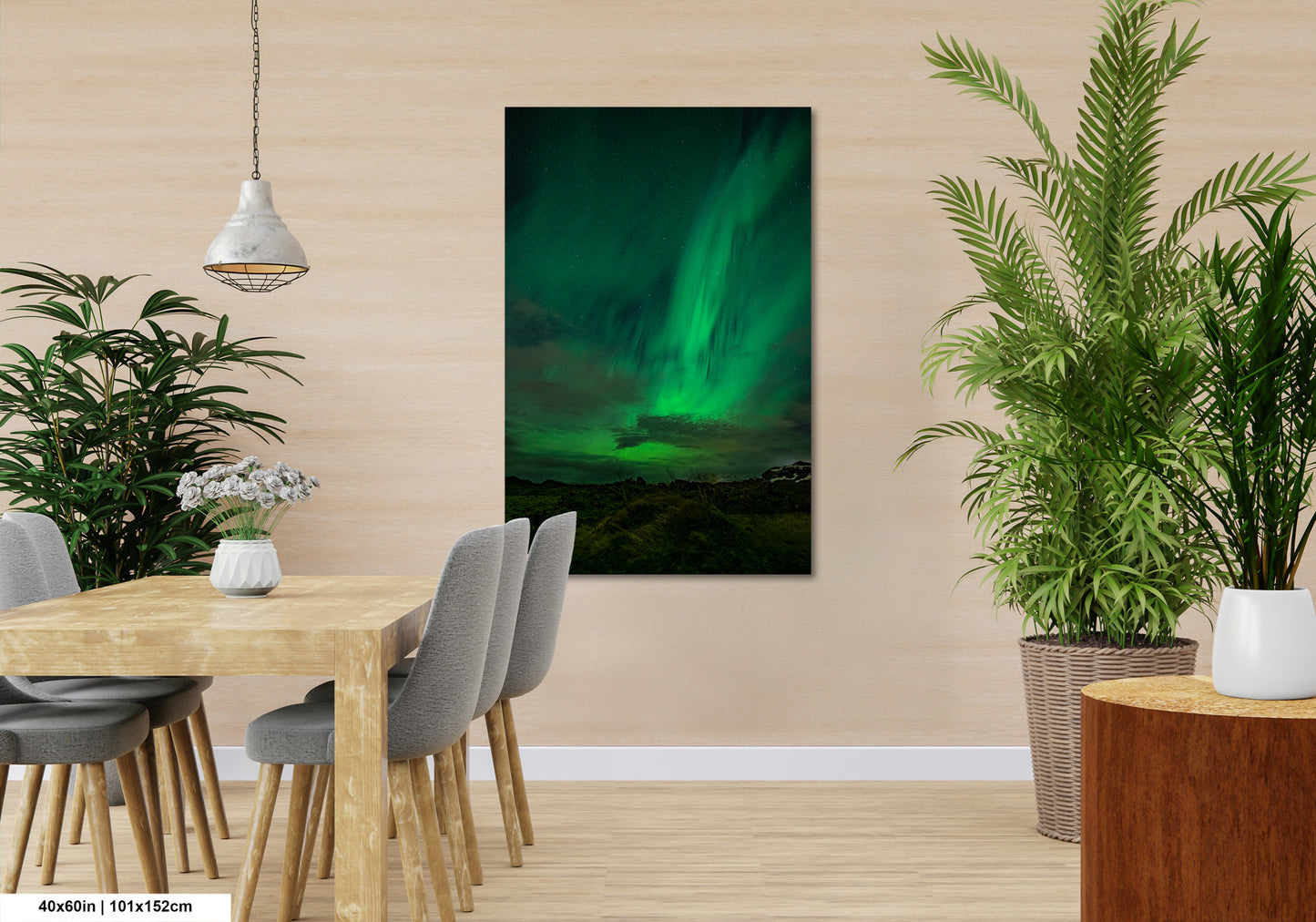 a serene indoor setting with a wooden dining table surrounded by gray chairs, a hanging light fixture, and a large potted plant. A large framed picture of the Aurora Borealis, or Northern Lights, is displayed on the wall, creating a captivating and natural atmosphere in the room.