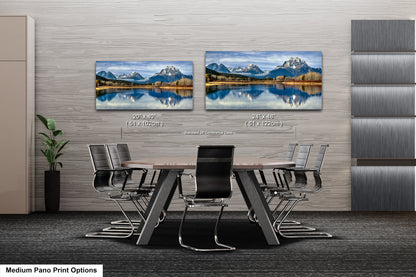 a modern office space with a large wall displaying two framed landscape paintings depicting a serene mountain lake scene. The paintings are hung at eye level, creating a focal point in the room. The office space includes a wooden table surrounded by chairs, and a potted plant is visible in the corner.