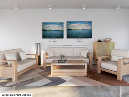 a modern living room with a large sofa, two chairs, and a coffee table. There are two framed landscape paintings on the wall above the seating area, depicting a serene lake and a blue sky with clouds. The room has a neutral color scheme with white walls and a wooden floor.