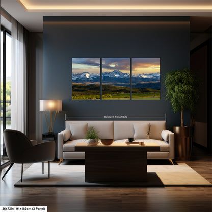 A modern living room with a large wall-mounted landscape painting depicting a scenic mountain range at sunset. The painting is framed in a three-panel format and is the focal point of the room. The room is furnished with a sofa, armchair, and coffee table, creating a cozy and inviting atmosphere.