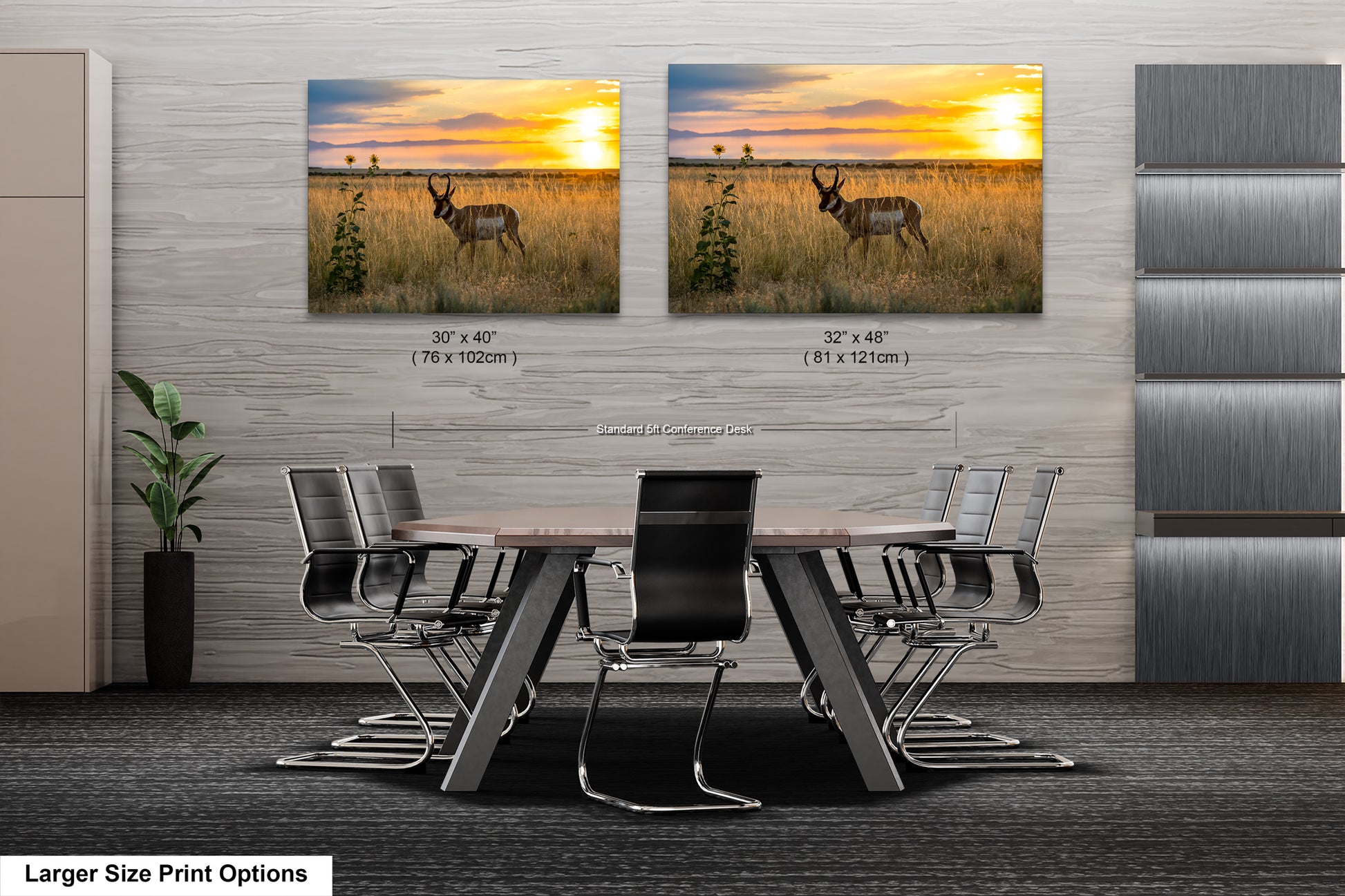 a modern office space with a large wooden table surrounded by black chairs. Above the table, there are two framed pictures of a gazelle in a grassy field, depicting a serene sunset. The pictures are of different sizes, with one being larger than the other. The office space has a minimalist design with gray walls and a gray carpet.