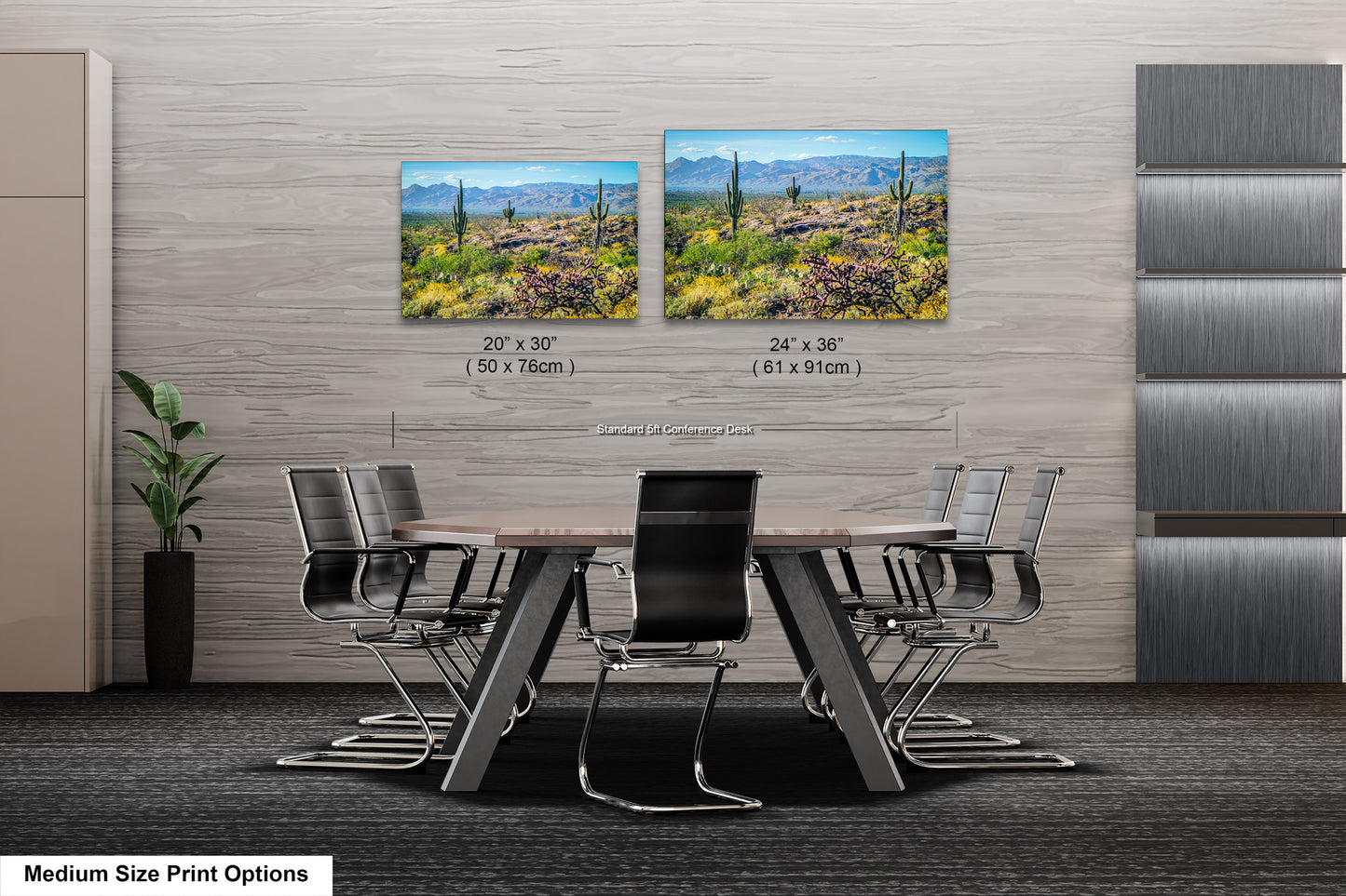 a modern office space with a large wooden table surrounded by black chairs. Two framed landscape paintings are displayed on the wall above the table, depicting a desert scene with mountains in the background.