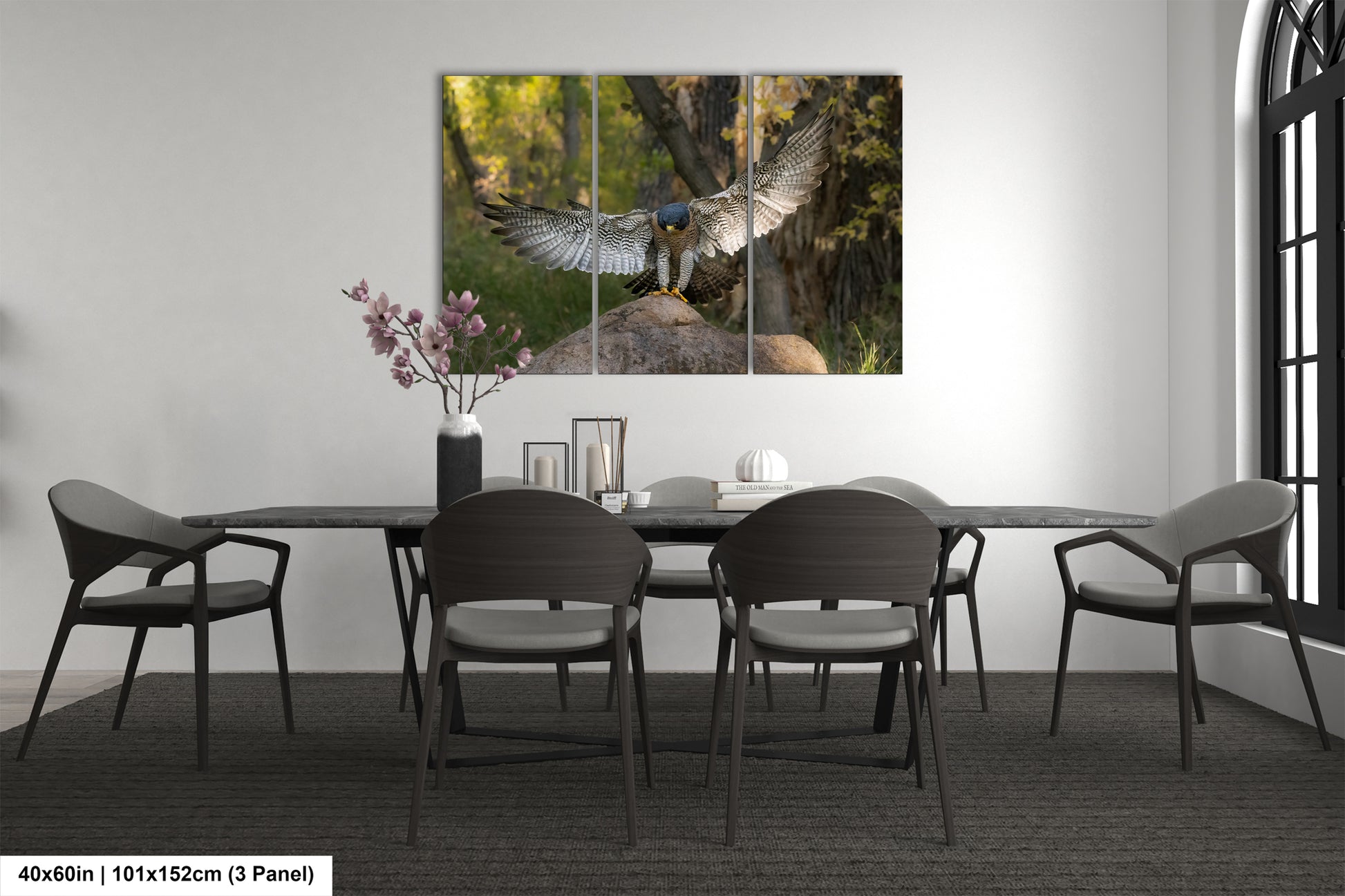 a modern dining room with a large painting of a bird of prey, possibly a hawk, on the wall above a table with chairs. The painting is divided into three panels, creating a dynamic and visually engaging display. The room has a minimalist and clean design, with a gray color scheme and a vase of flowers on the table adding a touch of nature to the space.