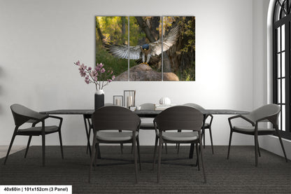 a modern dining room with a large painting of a bird of prey, possibly a hawk, on the wall above a table with chairs. The painting is divided into three panels, creating a dynamic and visually engaging display. The room has a minimalist and clean design, with a gray color scheme and a vase of flowers on the table adding a touch of nature to the space.
