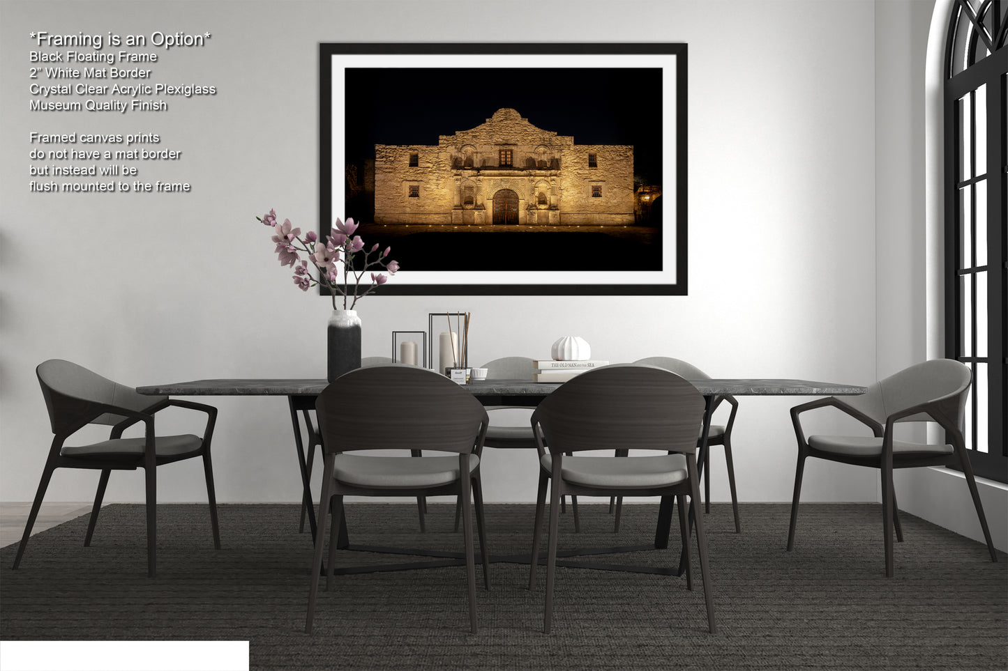 a modern dining room with a large framed photograph of the Alamo in the background, a black table with four chairs, and a vase of pink flowers on the table.