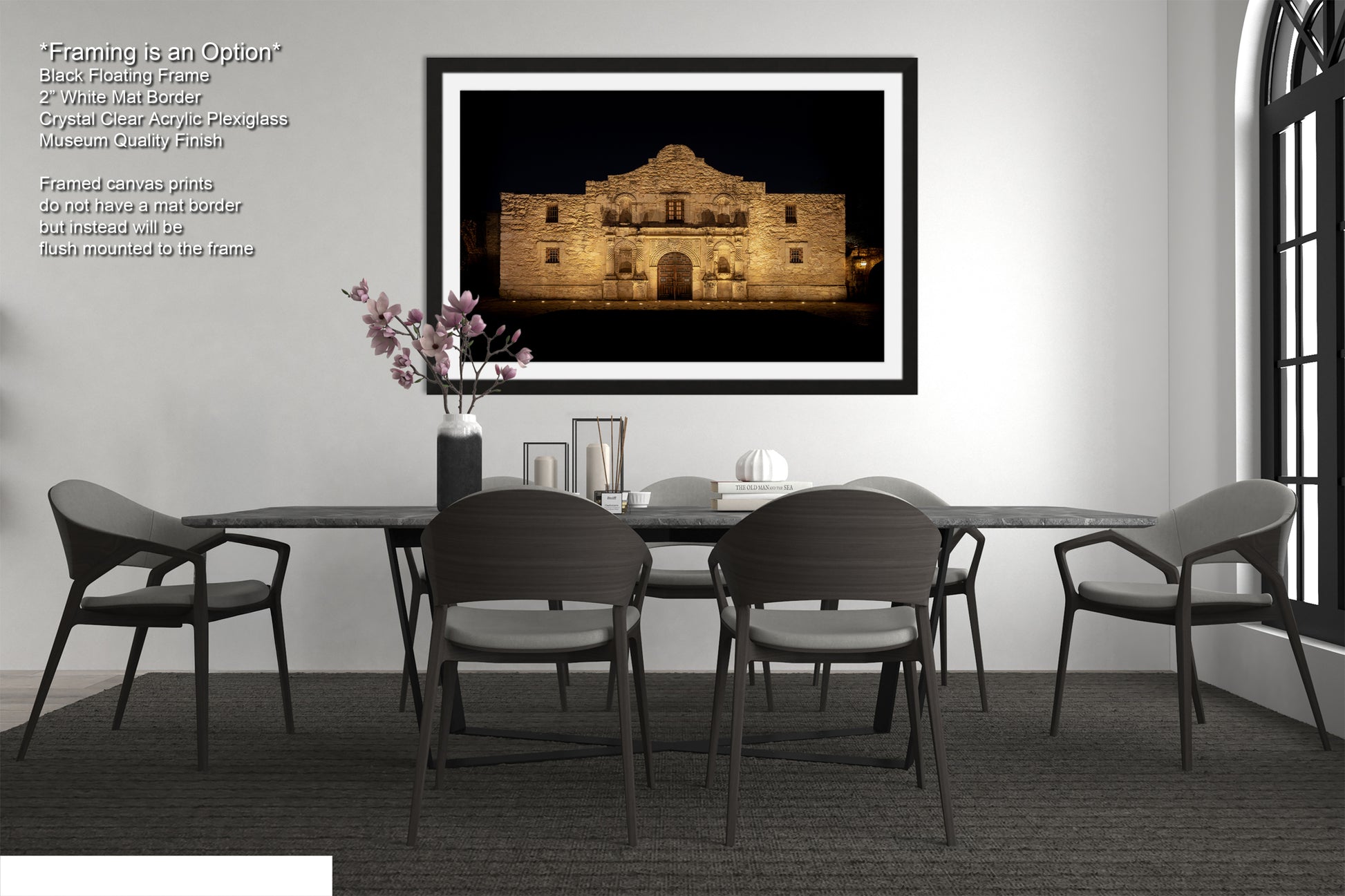 a modern dining room with a large framed photograph of the Alamo in the background, a black table with four chairs, and a vase of pink flowers on the table.