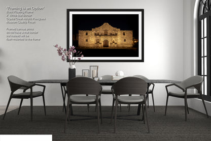 a modern dining room with a large framed photograph of the Alamo in the background, a black table with four chairs, and a vase of pink flowers on the table.