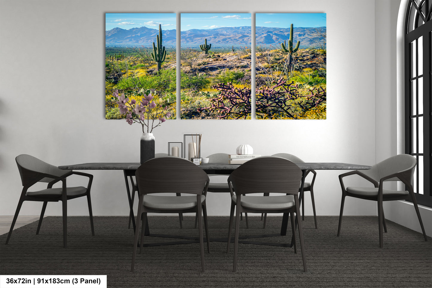 The image is a modern dining room with a large, three-panel landscape painting depicting a desert scene with cacti and mountains in the background. The painting is hung on the wall above a black dining table surrounded by chairs.